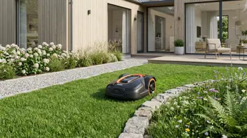 Robotgräsklippare på gräsmattan intill en grusgång vid ett modernt hus.