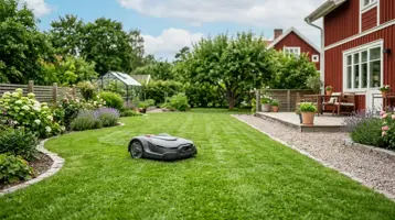 Robotgräsklippare på en randigt klippt gräsmatta framför ett rött hus.