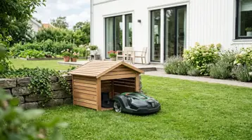 Robotgräsklippare på gräsmattan bredvid ett litet trähus som skyddar laddstationen.