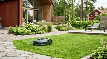 Robotgräsklippare på gräsmattan intill en uteplats i en svensk trädgård.